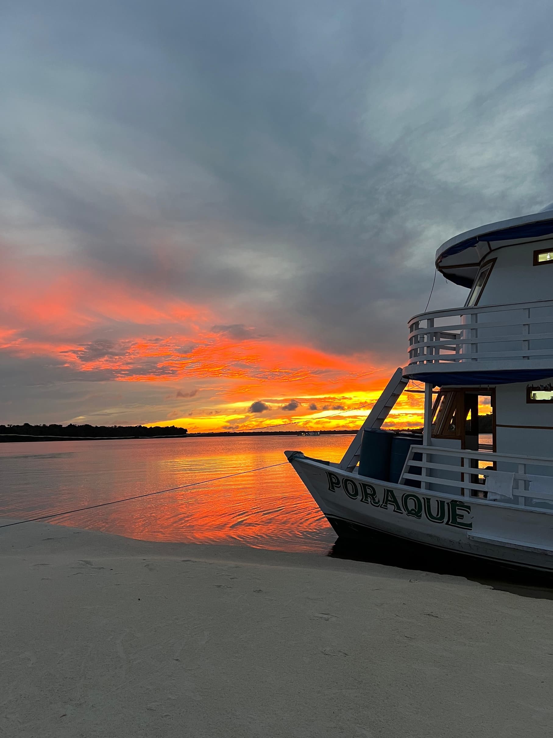 Casco do Barco Poraquê encostado na praia ao pôr do sol no Rio Negro
